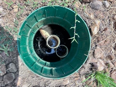 Open green septic tank riser, looking down at the pipes inside